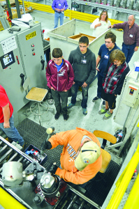A group of students looks on as a Bristol Compressors employee uses a mallet to finesse a piece into place.