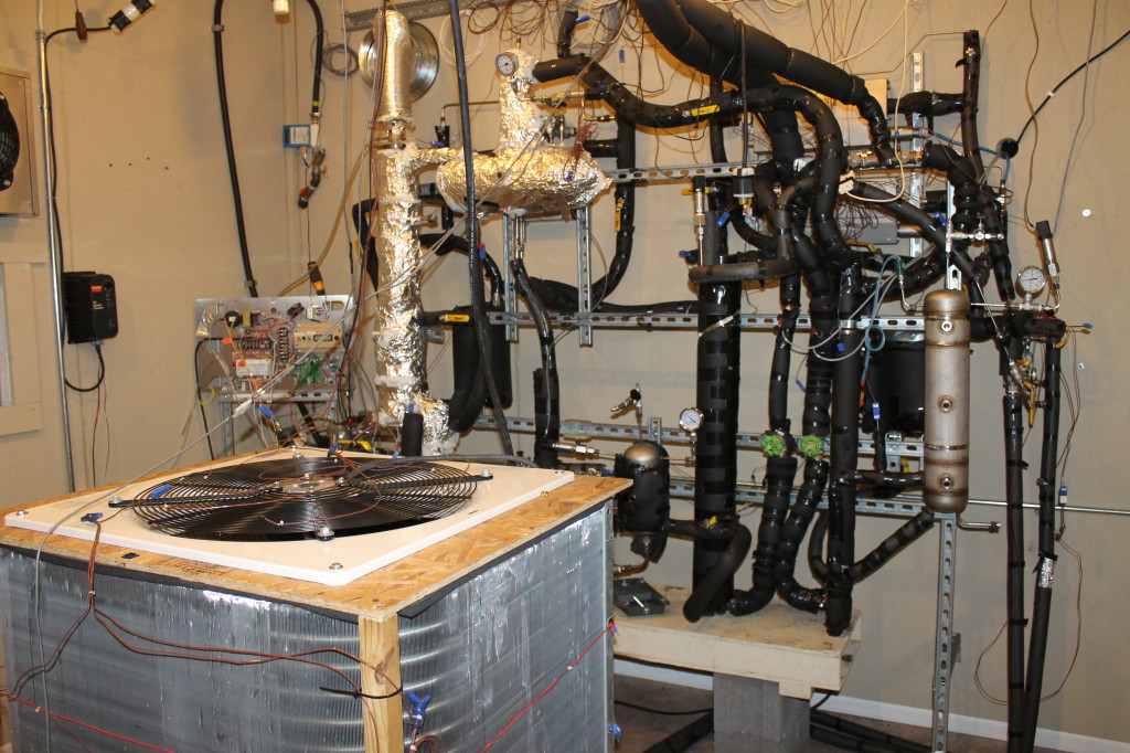 The shell of a prototype gas heat pump for home heating, foreground, in the shop's "breadboard room" where various testing occurs.